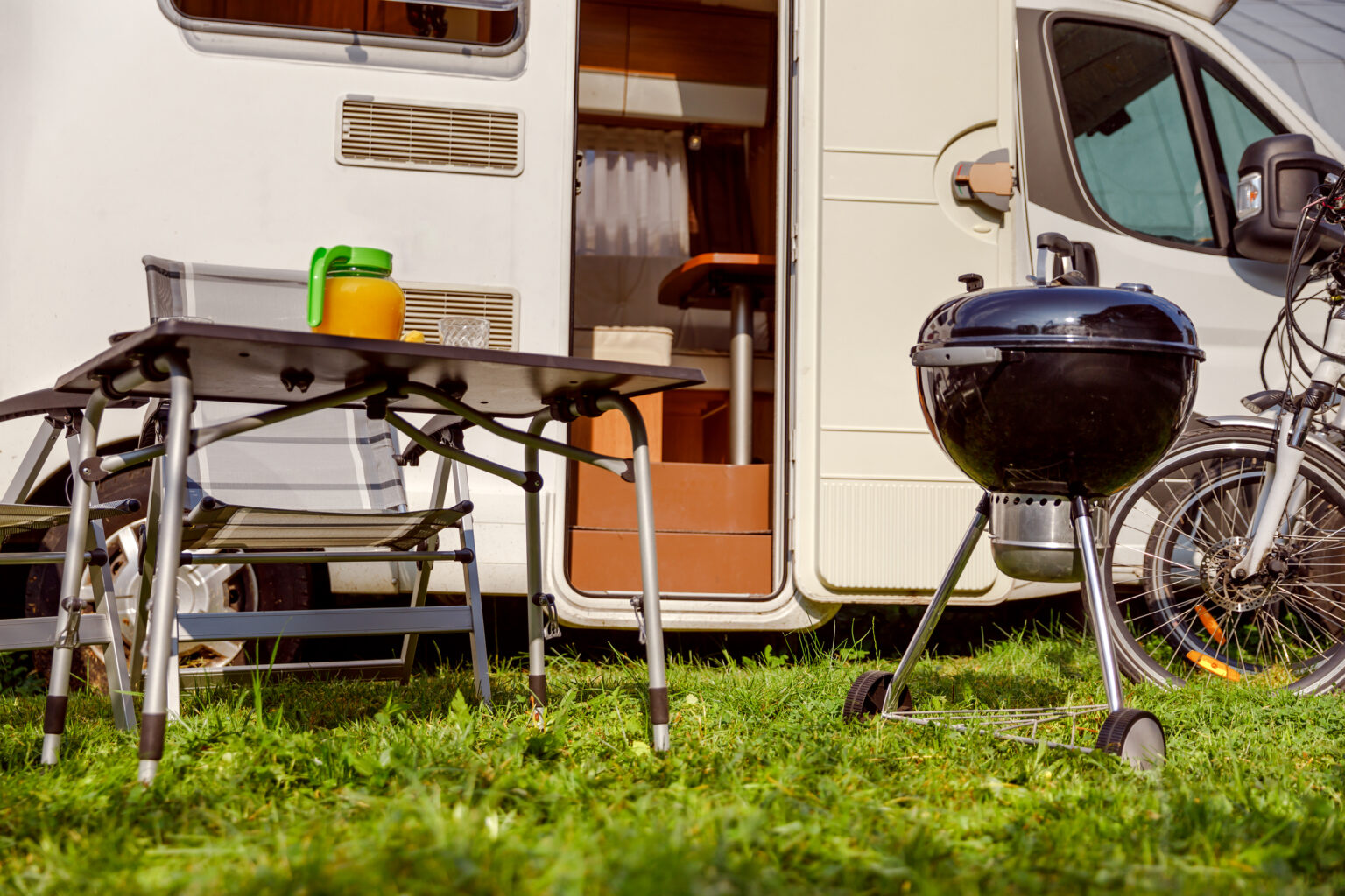 rv parked at campsite with bicycles, grill, table and chairs