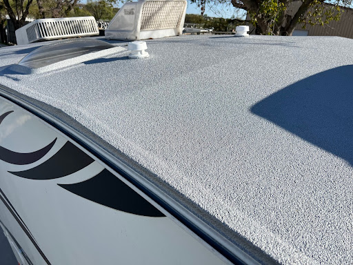 Close-up of an RV roof coated with a textured, seamless ApexArmor spray lining, showing roof vents and A/C units under bright daylight.