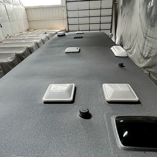 Close-up view of a freshly coated RV roof inside a workshop, featuring multiple vent covers and skylights. The seamless textured coating provides a protective waterproof finish, enhancing durability and insulation.
